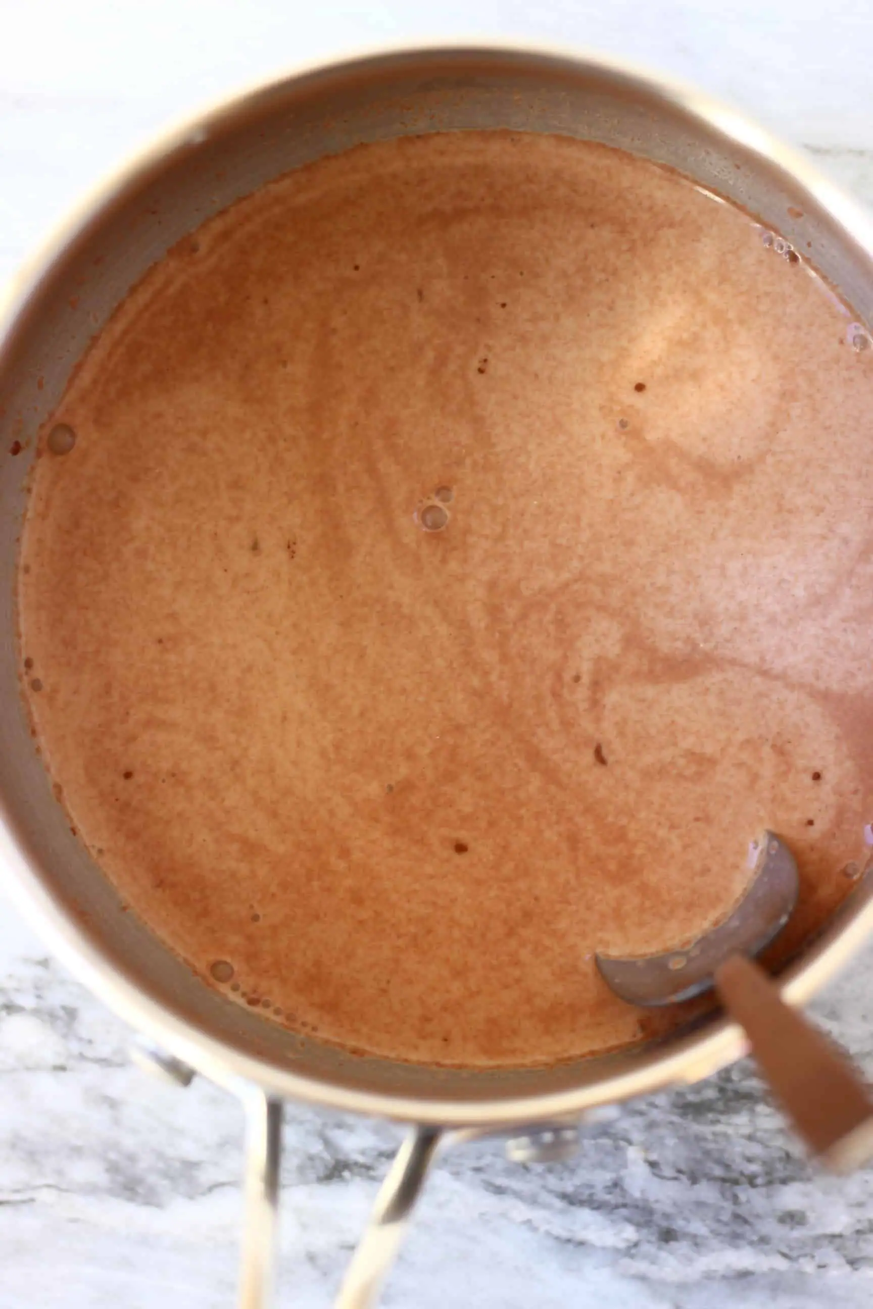 A pan with vegan chocolate milk and a spoon stirring in cornflour