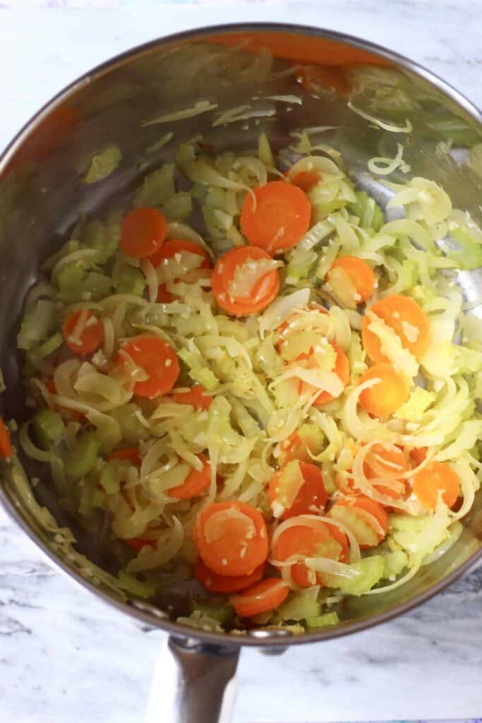 Photo of sliced onions, minced garlic, diced celery and sliced carrots in a silver saucepan