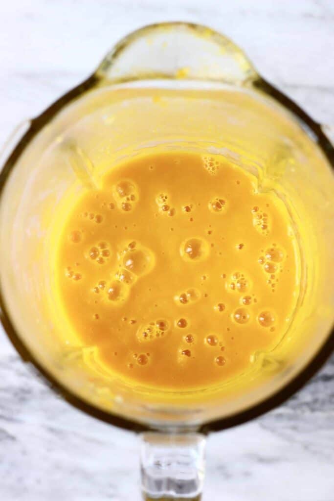 Photo of orange pumpkin soup in a glass blender against a marble background