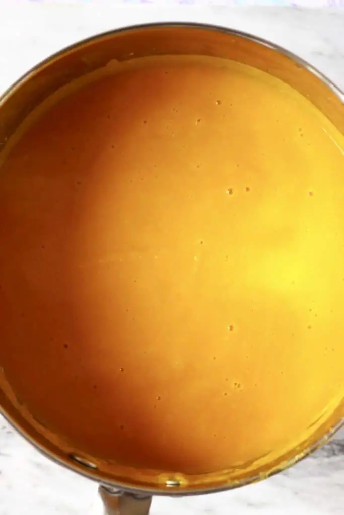 Photo of orange pumpkin soup in a silver saucepan against a marble background