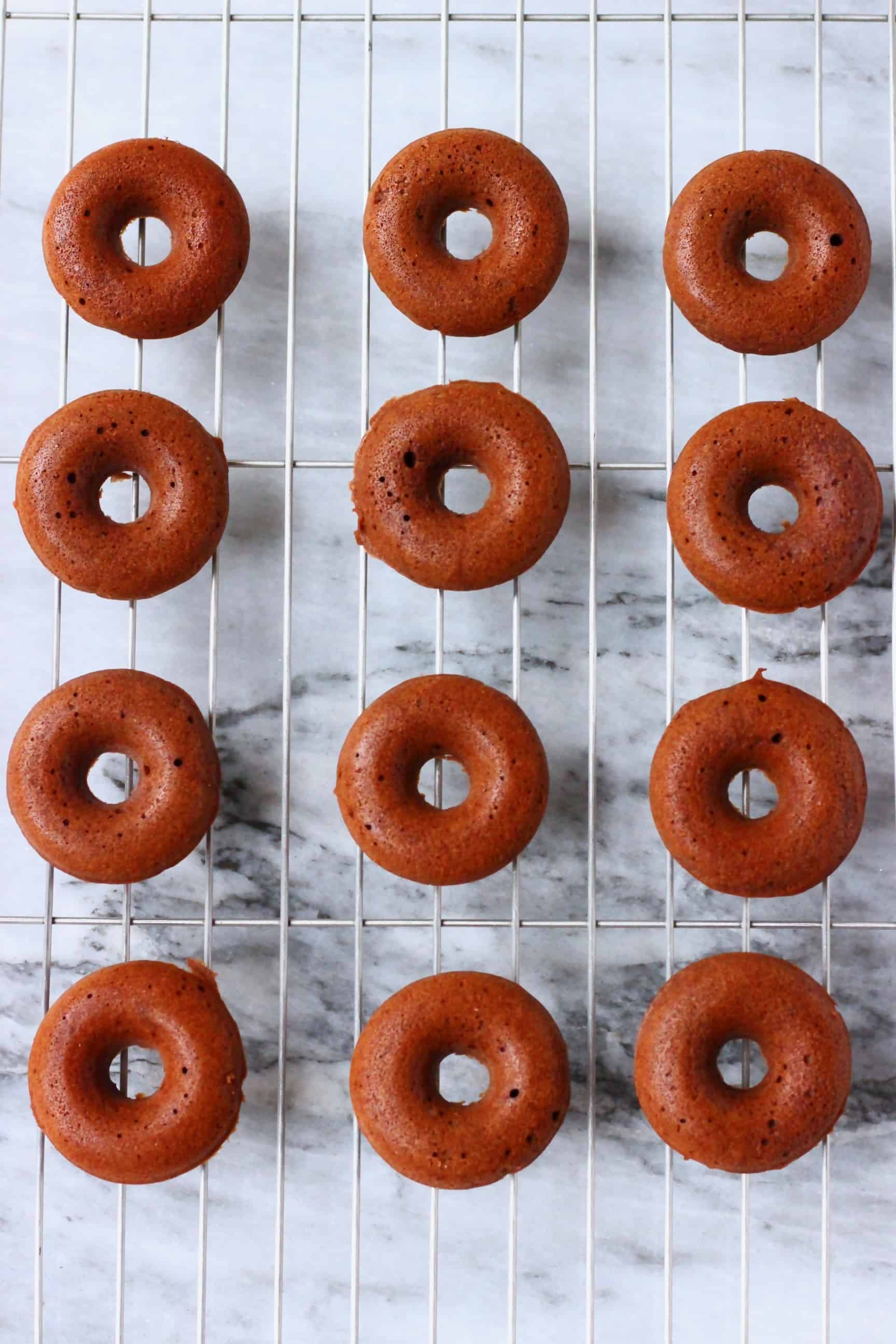 These Vegan Chocolate Baked Donuts are moist and fluffy and covered in a shiny chocolate glaze. A perfect snack or dessert for parties! Egg-free, dairy-free, gluten-free and refined sugar free. #rhiansrecipes #donuts #vegan #glutenfree #dairyfree Chocolate mini donuts on a wire rack against a marble background