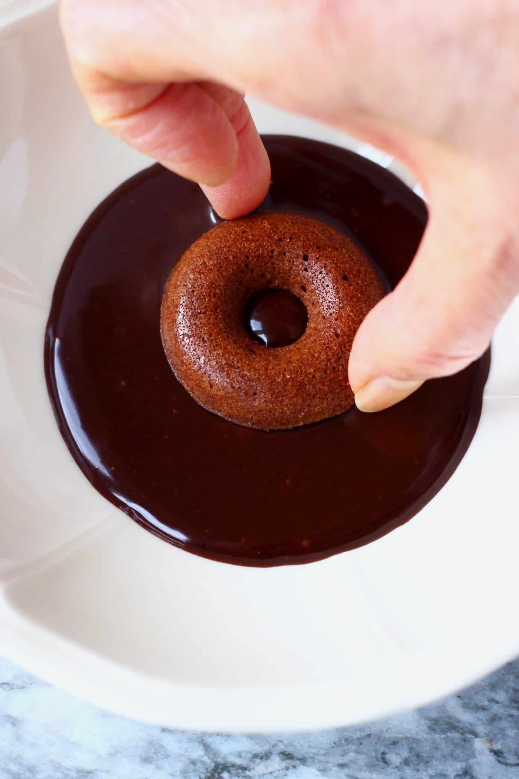 A mini chocolate donut being dipped into a white bowl of chocolate glaze