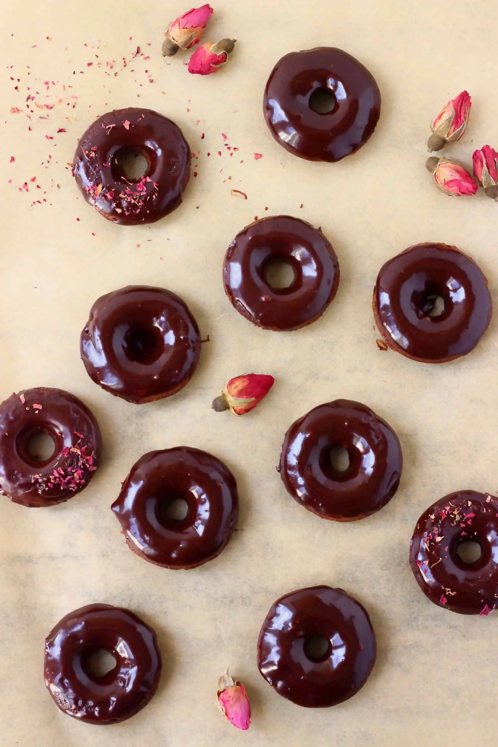 Chocolate glazed mini chocolate donuts on a sheet of brown baking paper decorated with dried roses