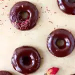 Chocolate glazed mini chocolate donuts on a sheet of brown baking paper decorated with dried roses
