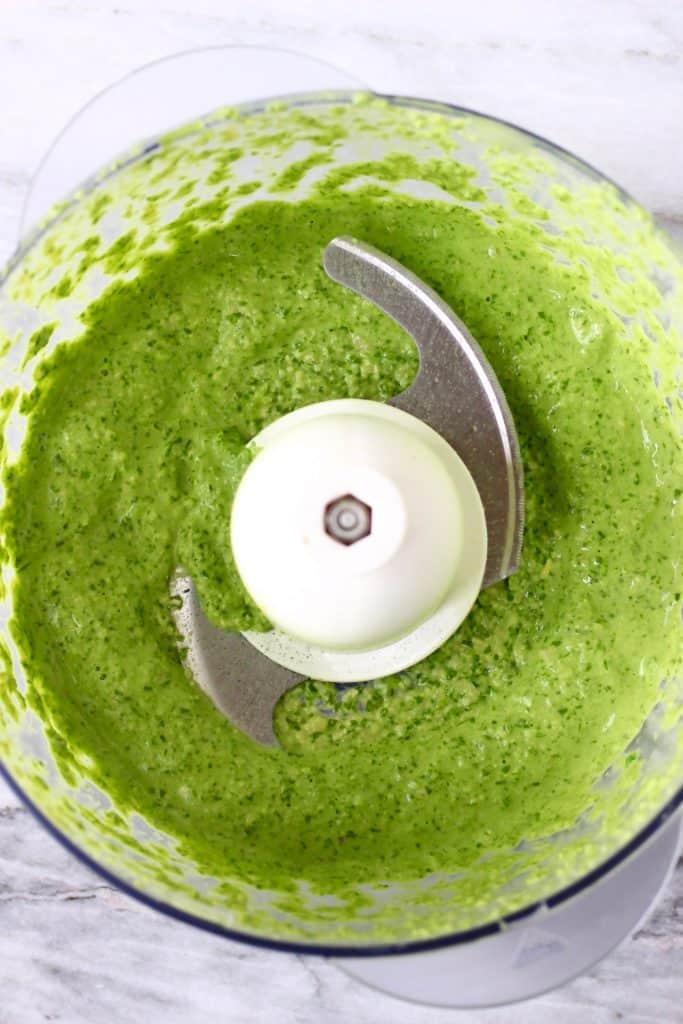 This Vegan Pesto Pasta is super easy to make, nutty and fragrant, and easily customisable! Includes a recipe for homemade vegan pesto. An easy plant-based dinner. Vegetarian, dairy-free, egg-free, gluten-free. #rhiansrecipes #pesto #pasta #vegan #glutenfree #dairyfree Green pesto in a food processor against a marble background