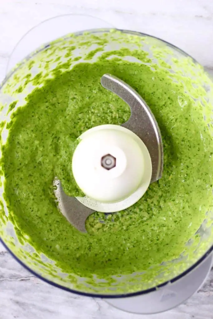 Green pesto in a food processor against a marble background