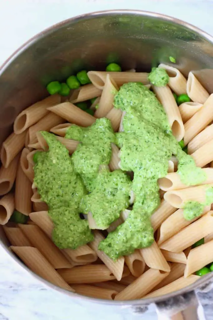 Cooked penne pasta and green peas in a silver saucepan with green pesto