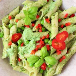 Penne pasta with pesto sauce, green peas and chopped red pepper in a beige bowl