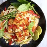 Vegan tofu pad Thai with vegetables and herbs and chopped peanuts in a black bowl