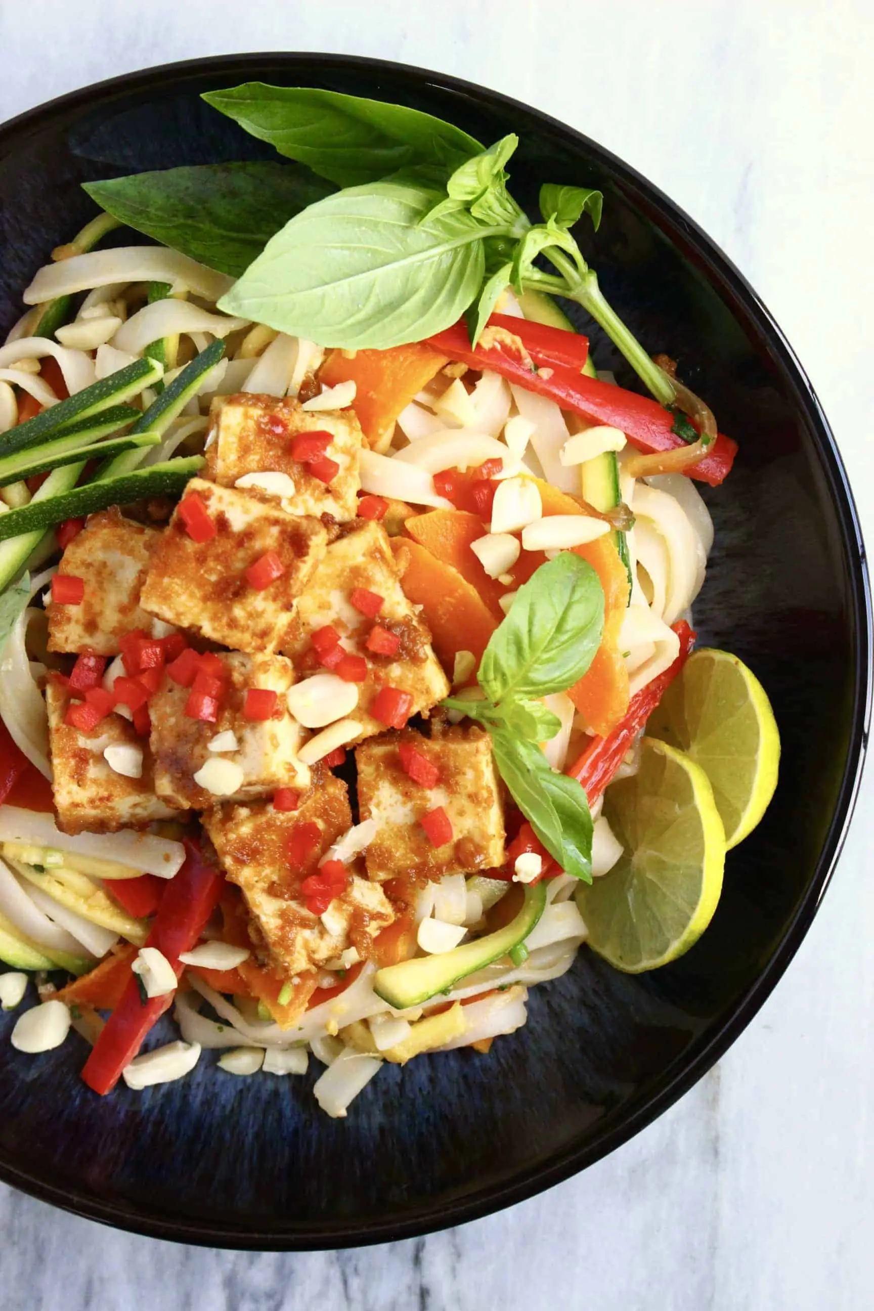 Vegan tofu pad Thai with vegetables and herbs and chopped peanuts in a black bowl