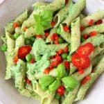 Penne pasta with pesto sauce, green peas and chopped red pepper in a beige bowl against a marble background