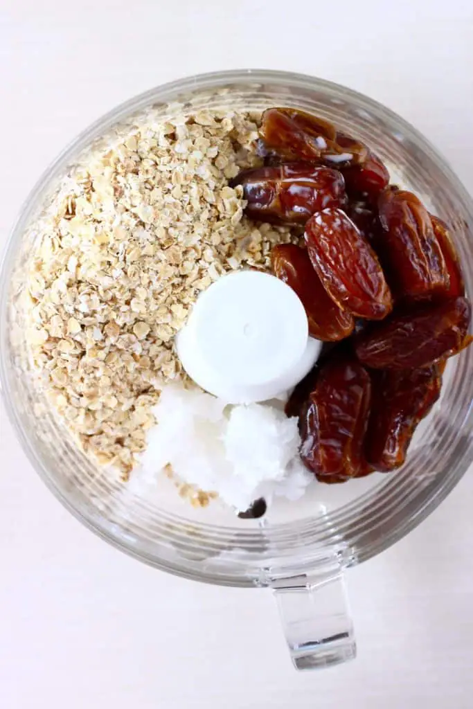 Oats, dates and coconut oil in a food processor against a white background