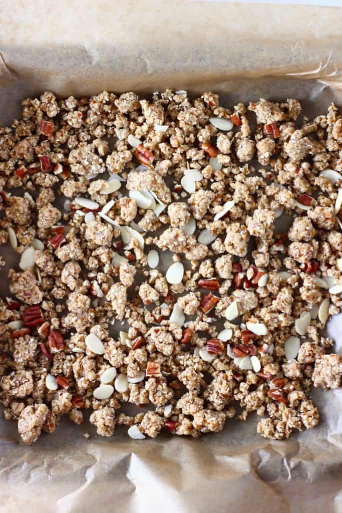 Raw granola mixture and pecan nuts on a baking tray lined with brown baking paper