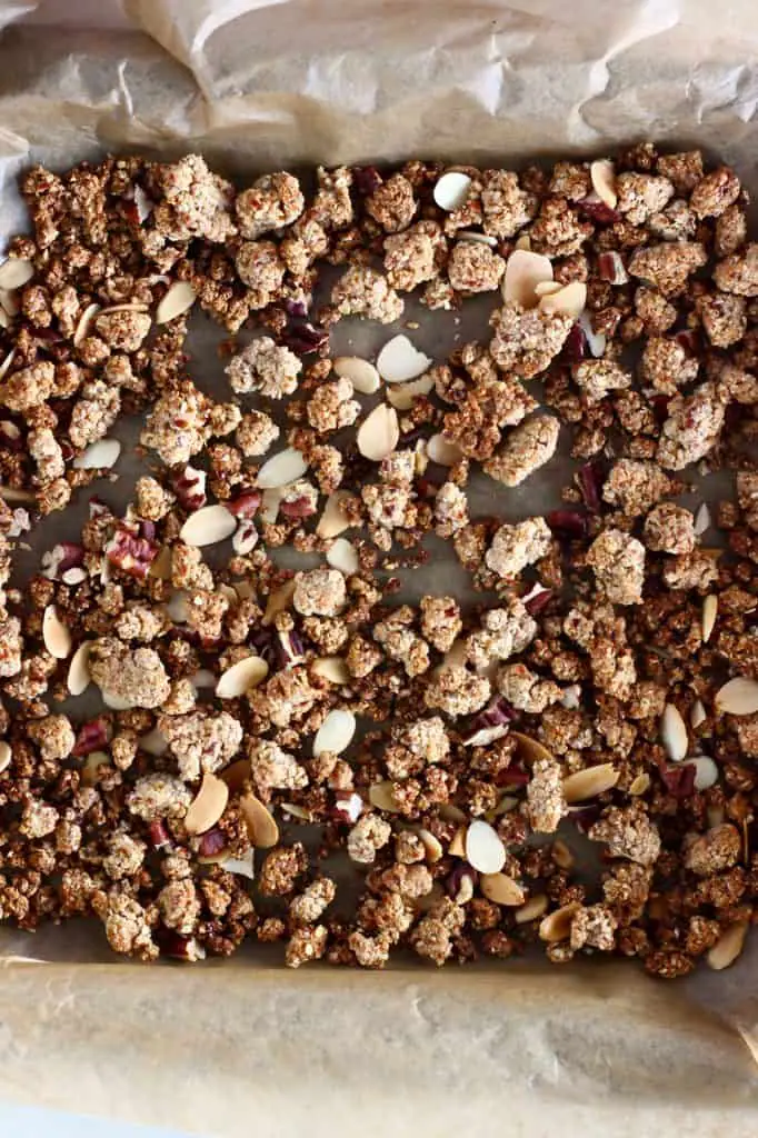 Brown granola with flaked almonds and pecan nuts on a baking tray lined with brown baking paper