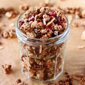Granola with pecan nuts and flaked almonds in a glass jar on a sheet of brown baking paper scattered with granola pieces