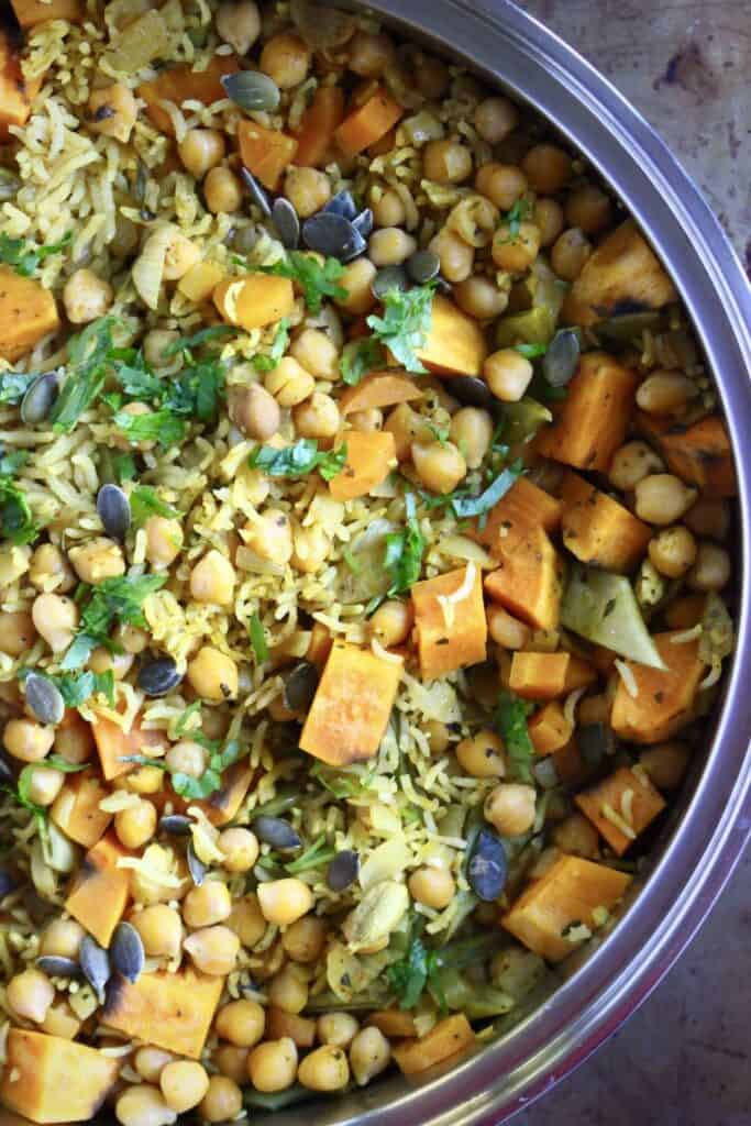 Photo of yellow biryani rice with chopped pumpkin, chickpeas and pumpkin seeds in a silver saucepan