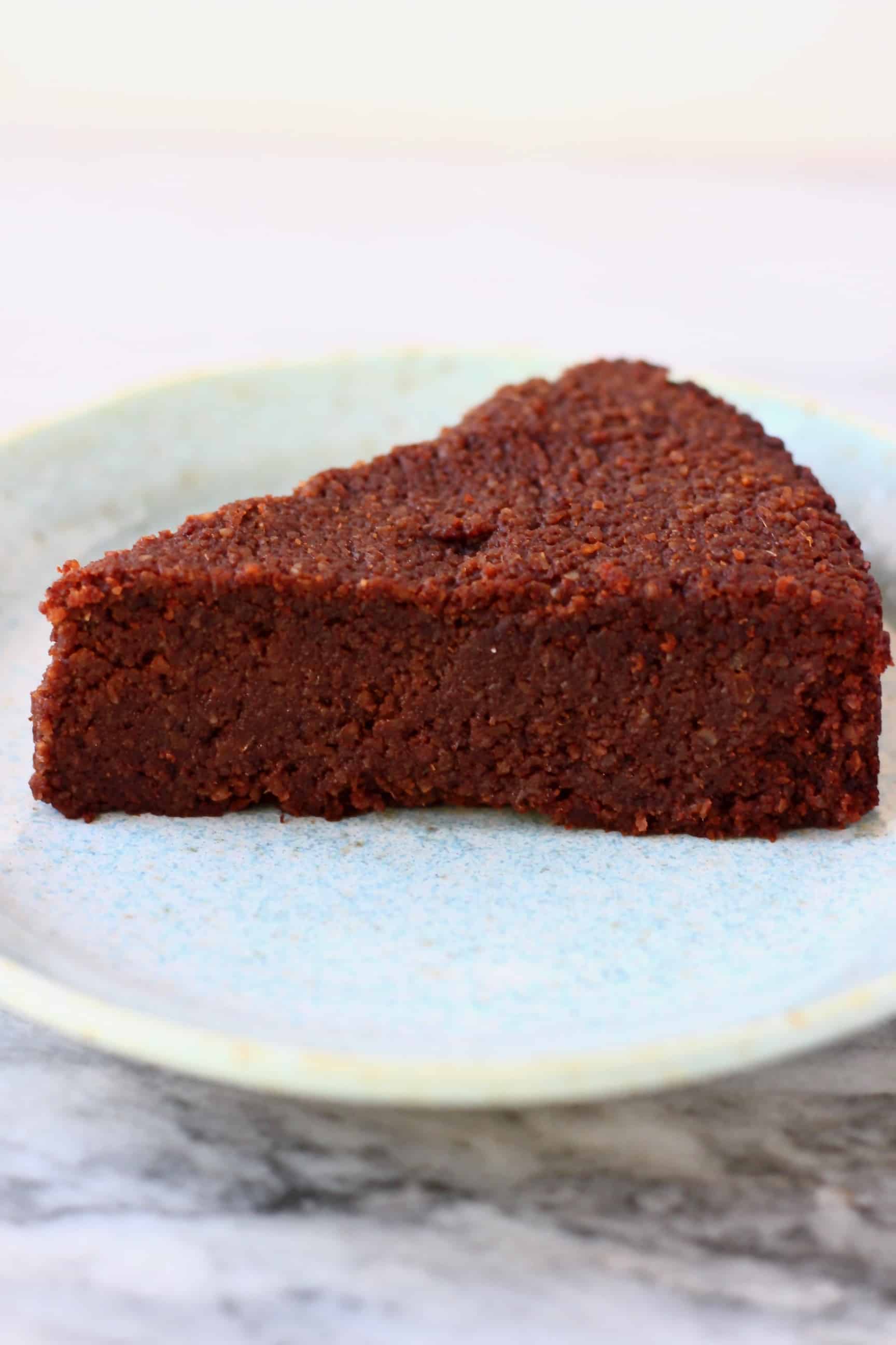 A slice of gluten-free vegan chocolate torte on a blue plate against a marble background