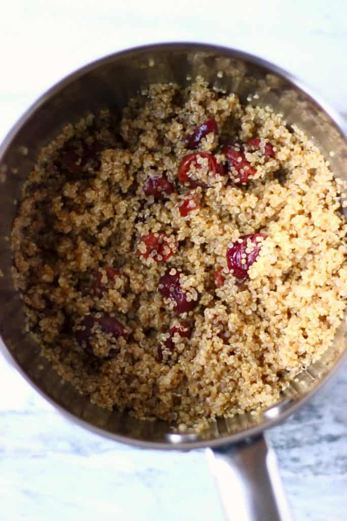 Cooked quinoa with dried cranberries in a silver saucepan against a marble background