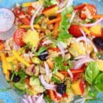 Quinoa salad with nectarine, dried cherries, sliced red onion and herbs on a blue plate against a pink background