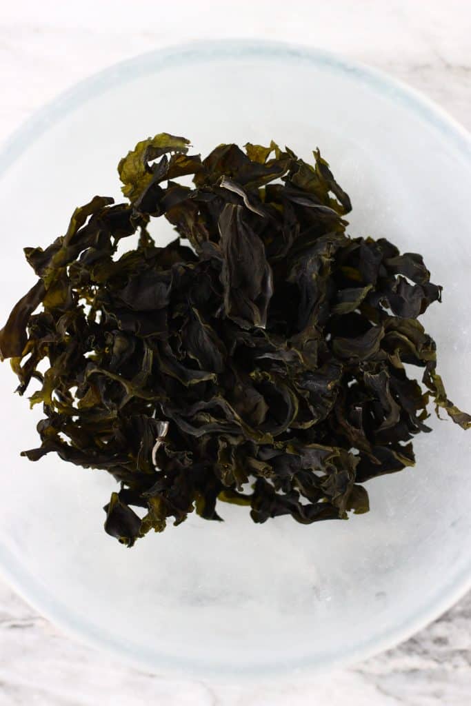 Dried wakame seaweed in a glass bowl against a marble background