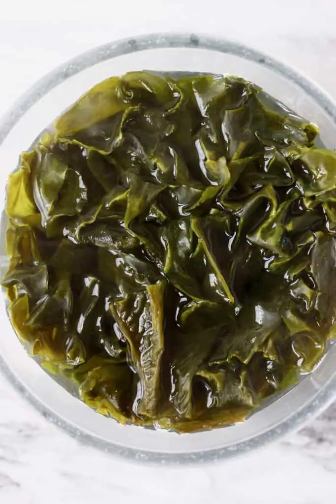 Wakame seaweed soaking in water in a glass bowl against a marble background