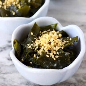 Seaweed salad topped with sesame seeds in a small blue bowl against a marble background