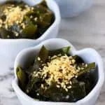 Seaweed salad topped with sesame seeds in three small blue bowls against a marble background