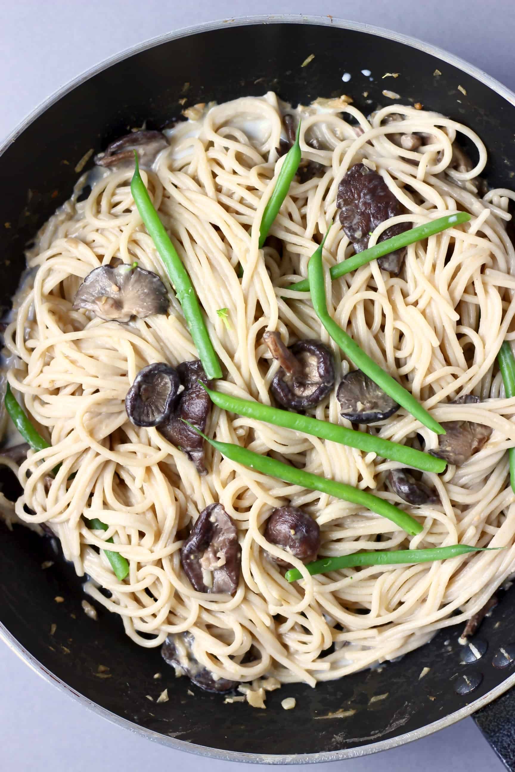 Spaghetti with creamy vegan miso pasta sauce, shiitake mushrooms and French beans in a black frying pan