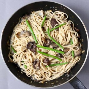 Spaghetti with creamy vegan miso pasta sauce, shiitake mushrooms and French beans in a black frying pan