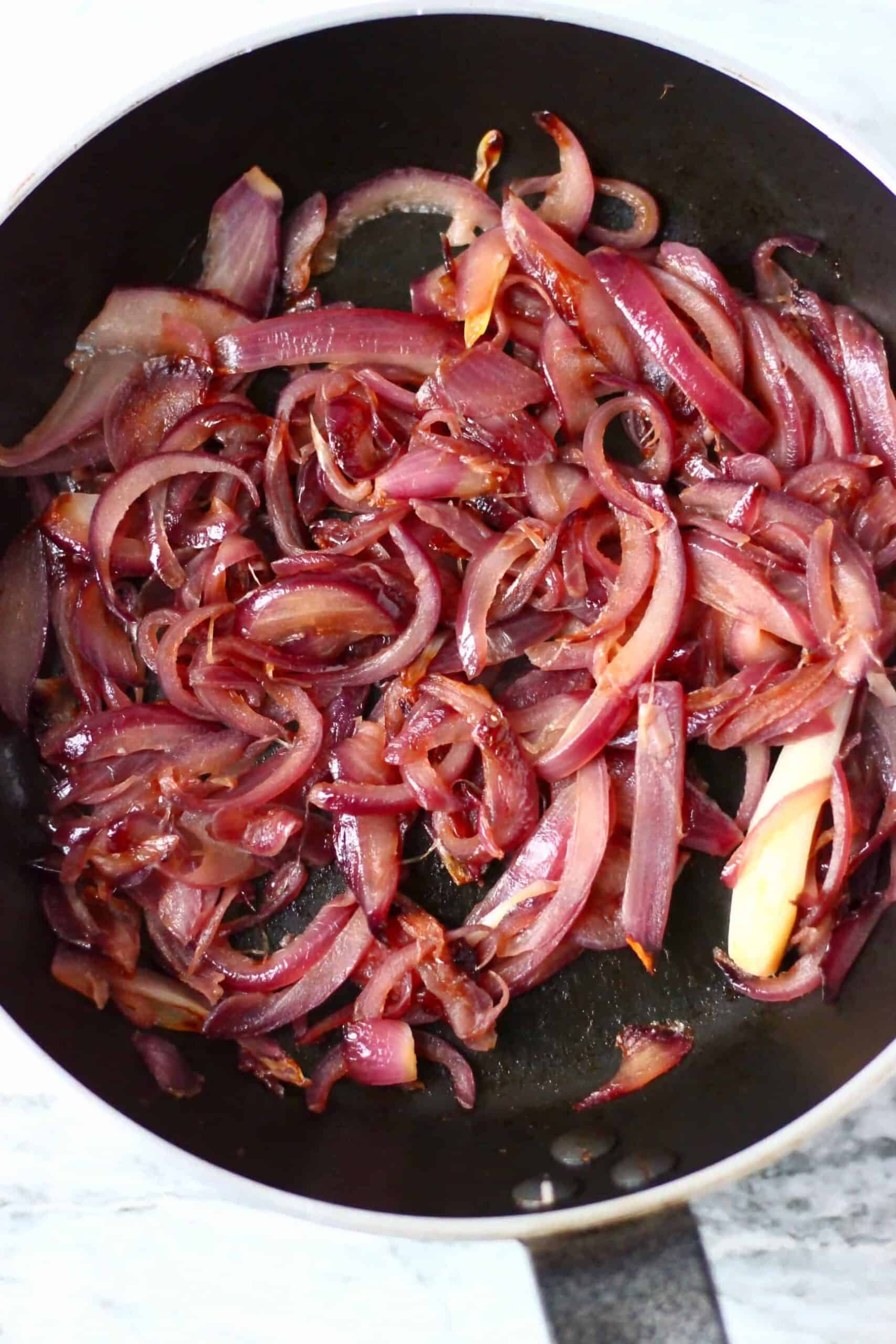Sliced red onions being cooked in a frying pan