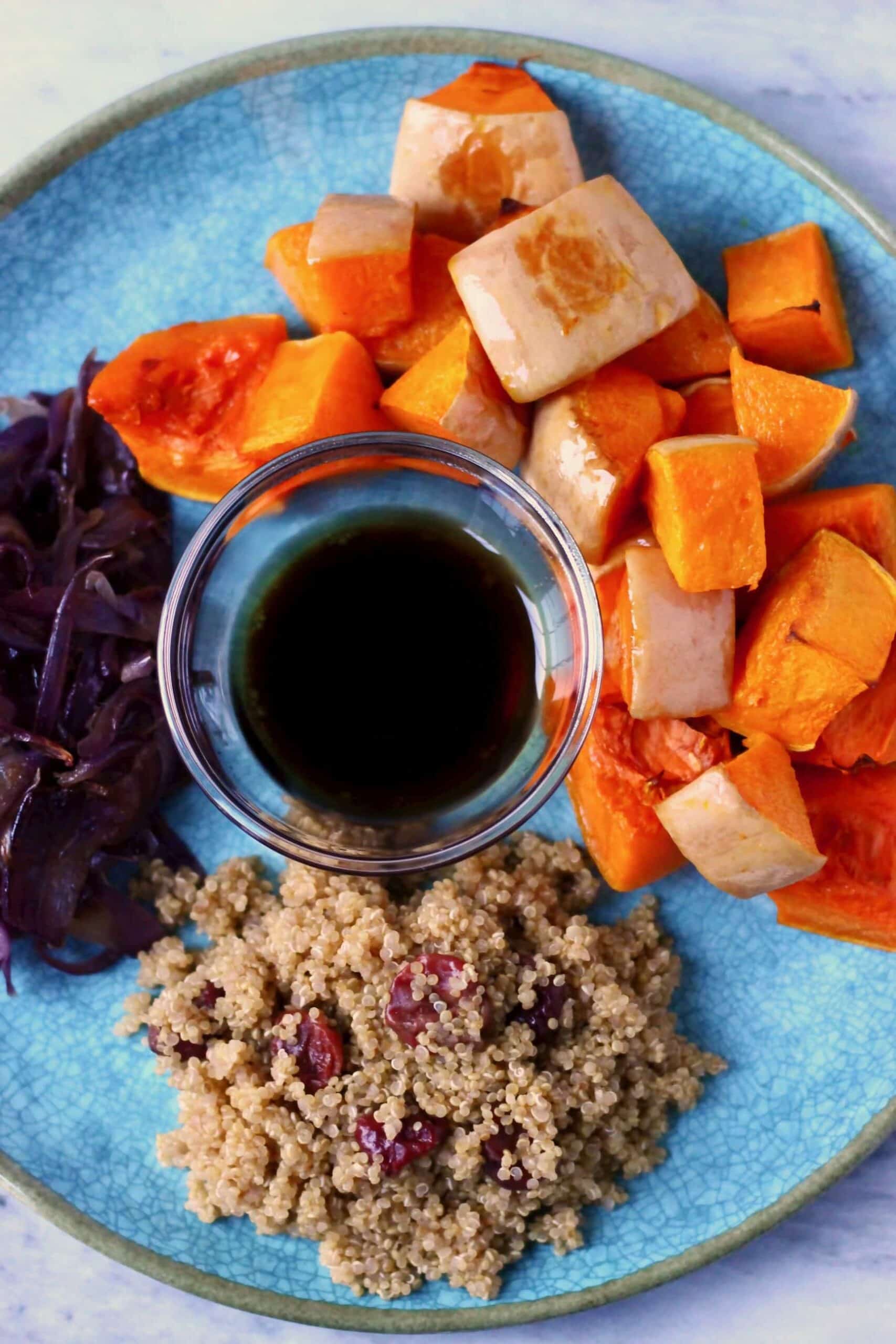 Roasted pumpkin cubes, cooked quinoa and dried cranberries, fried red onion slices and a small bowl of dressing on a plate