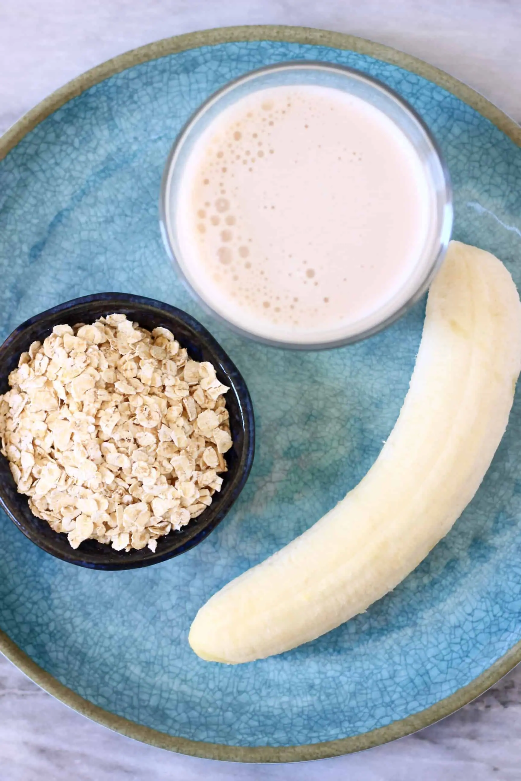 Oats, a peeled banana and a cup of almond milk on a blue plate
