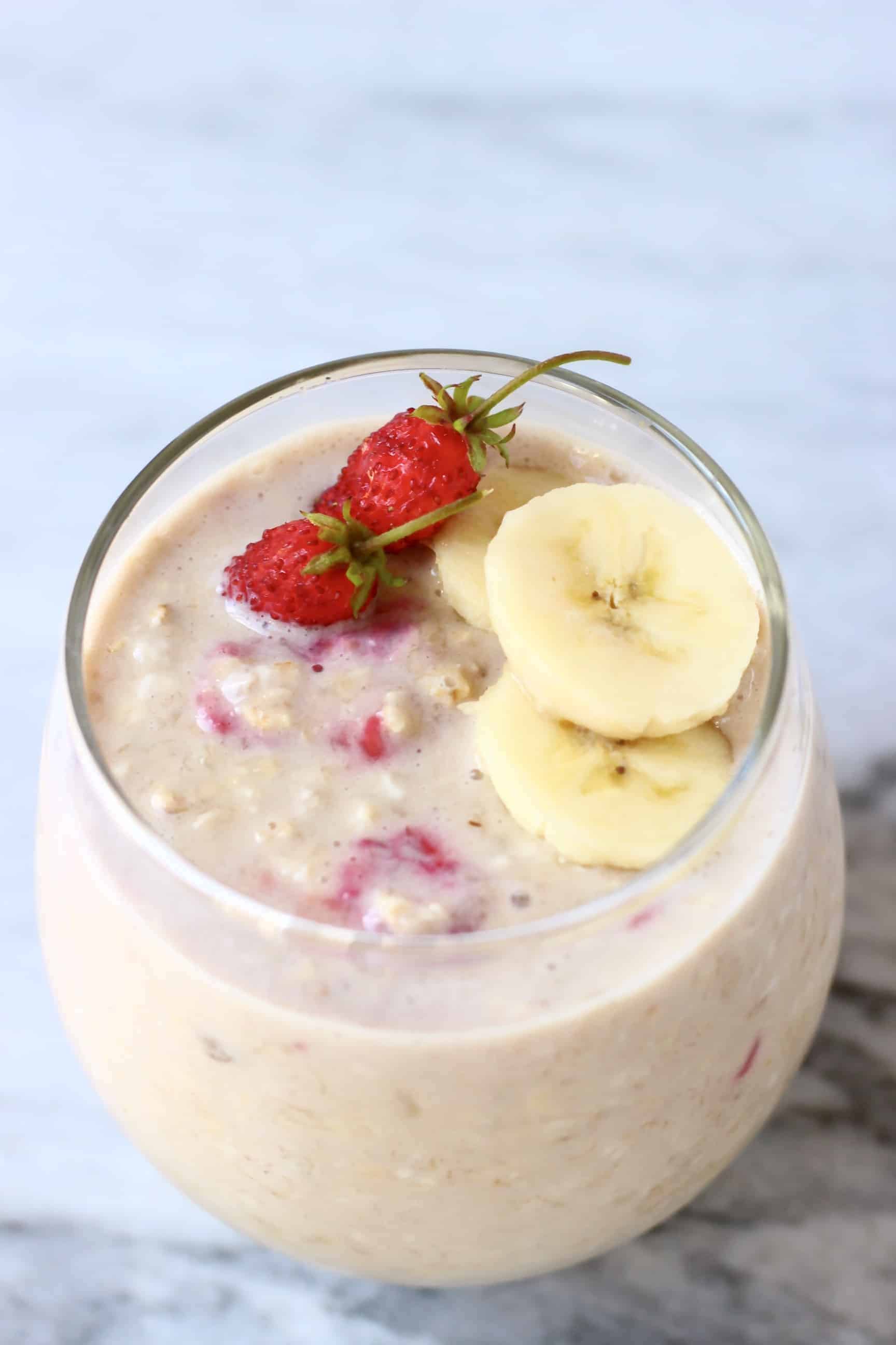 Banana overnight oats in a glass cup topped with sliced bananas and mini strawberries