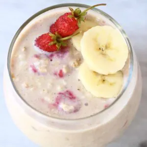 Banana overnight oats in a glass cup topped with sliced bananas and mini strawberries