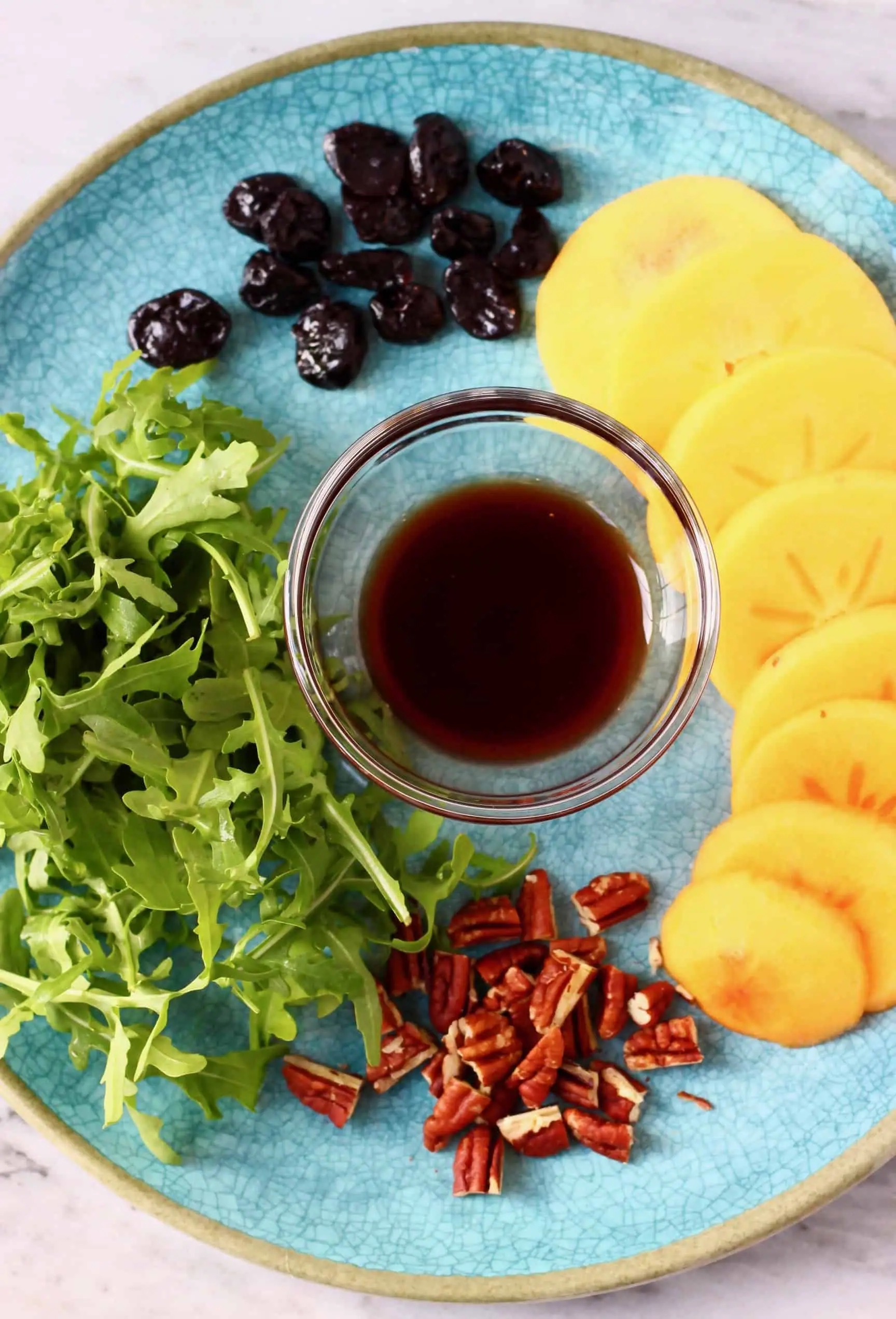 Persimmon slices, dried cherries, rocket, chopped pecan nuts and a brown dressing in a bowl on a plate