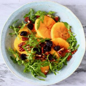 Persimmon salad with sliced persimmon, dried cherries, chopped pecan nuts and rocket in a bowl