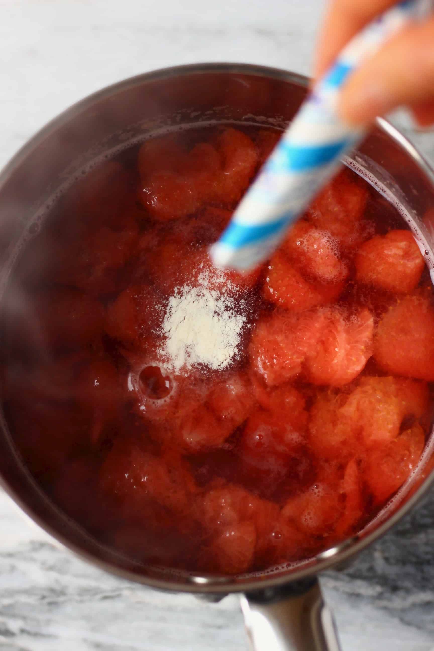Cooked strawberries and water in a pan with agar powder being sprinkled in