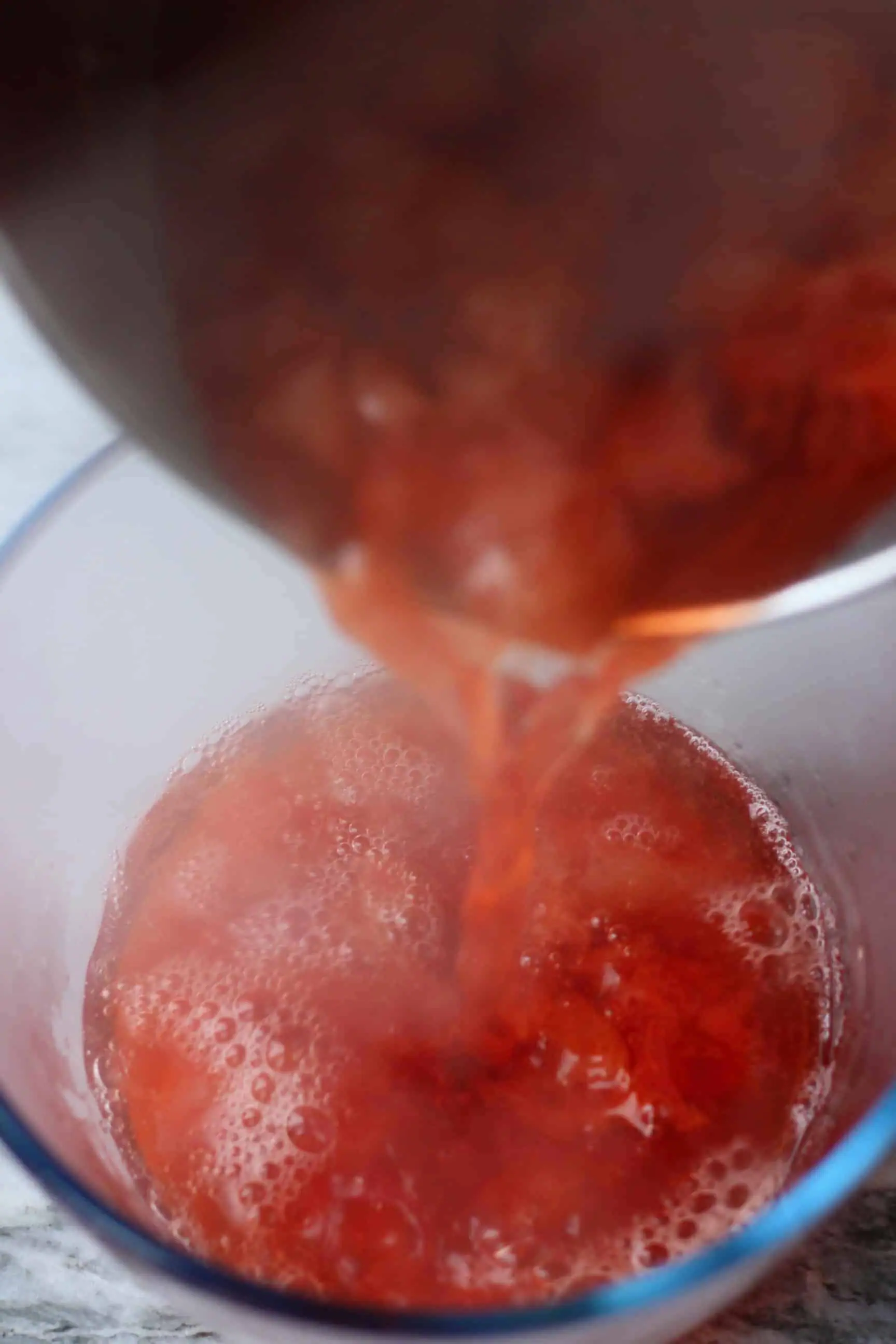 Cooked strawberries in water in a pan being poured into a glass trifle dish