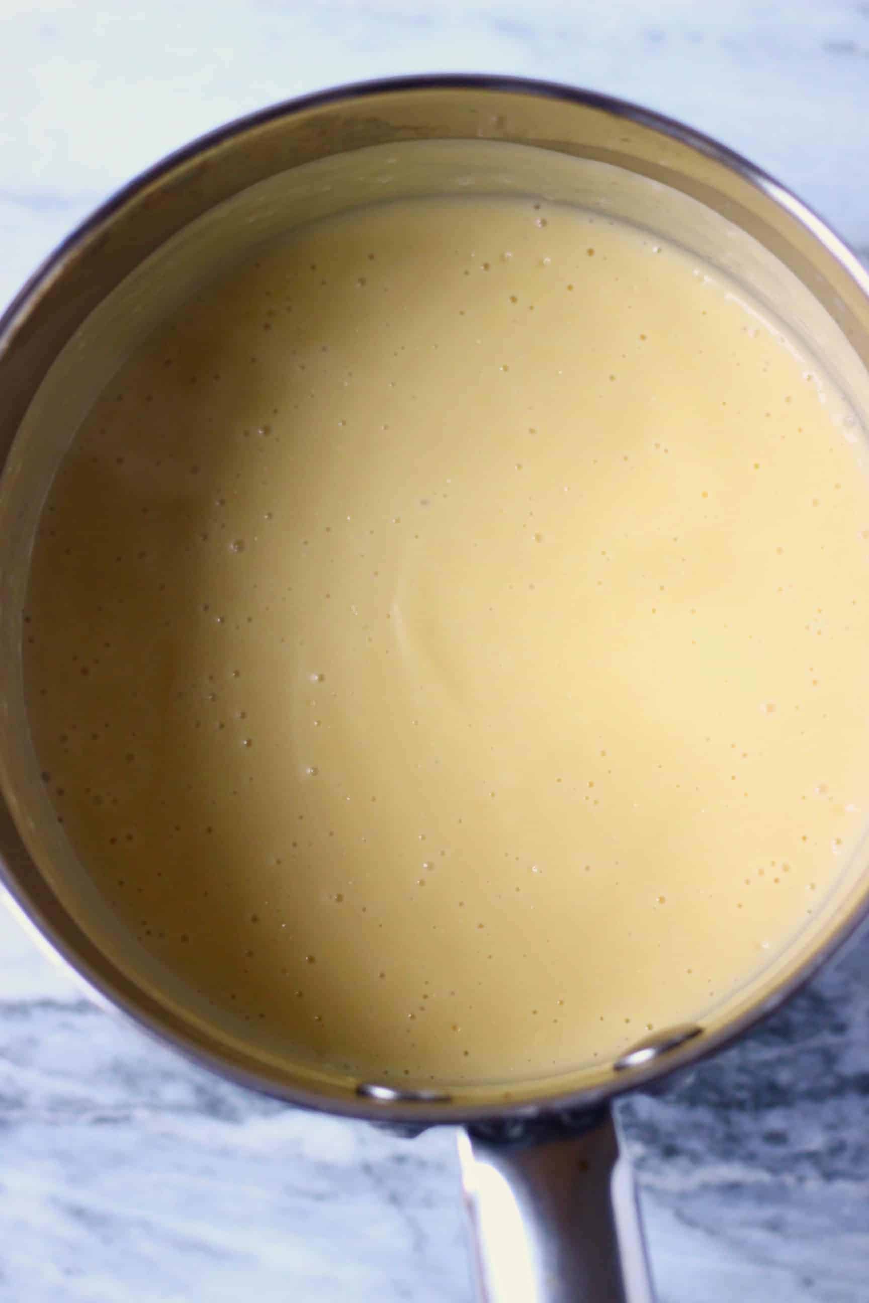 Yellow vegan custard in a pan against a marble background