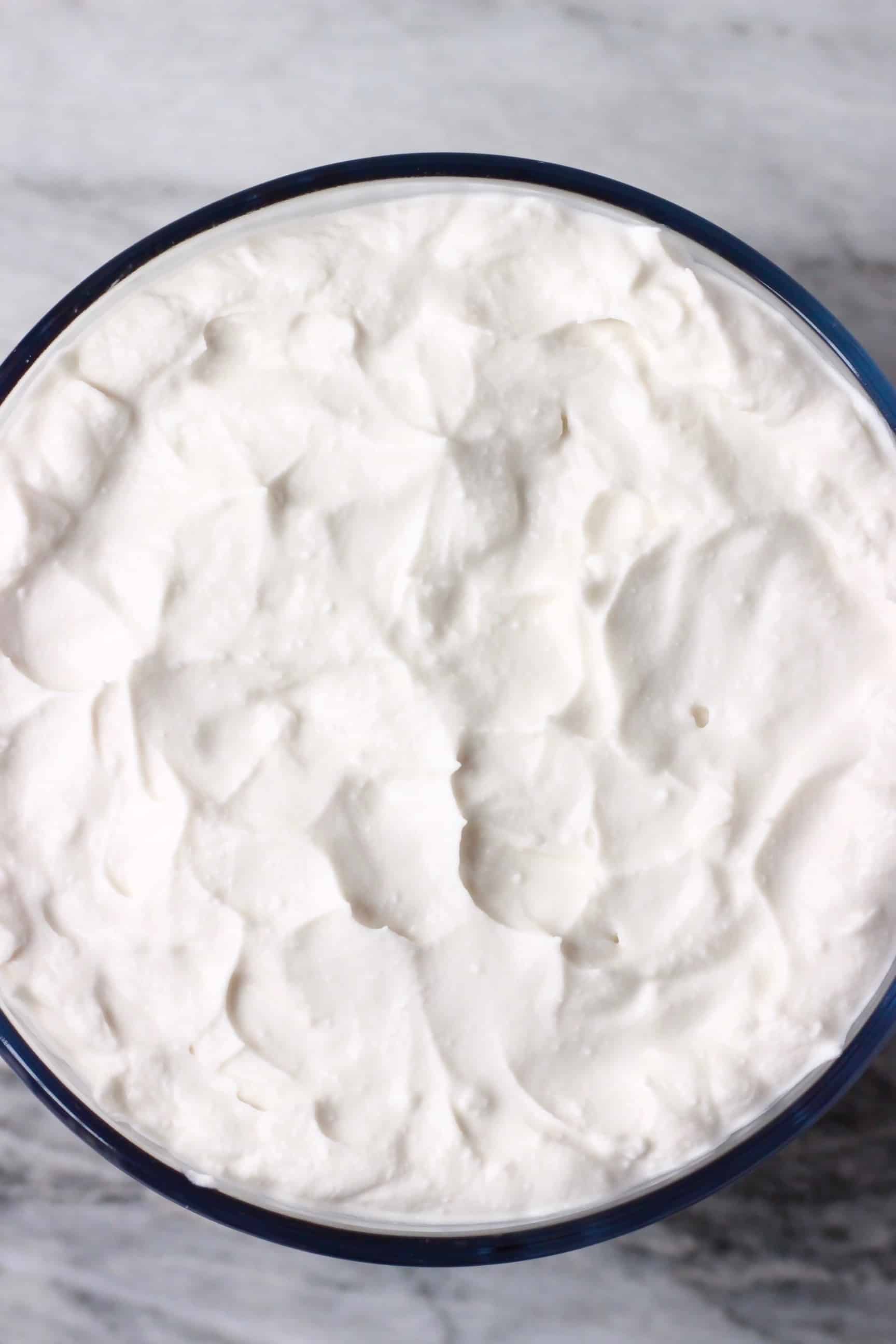 White vegan cream in a glass trifle dish against a marble background