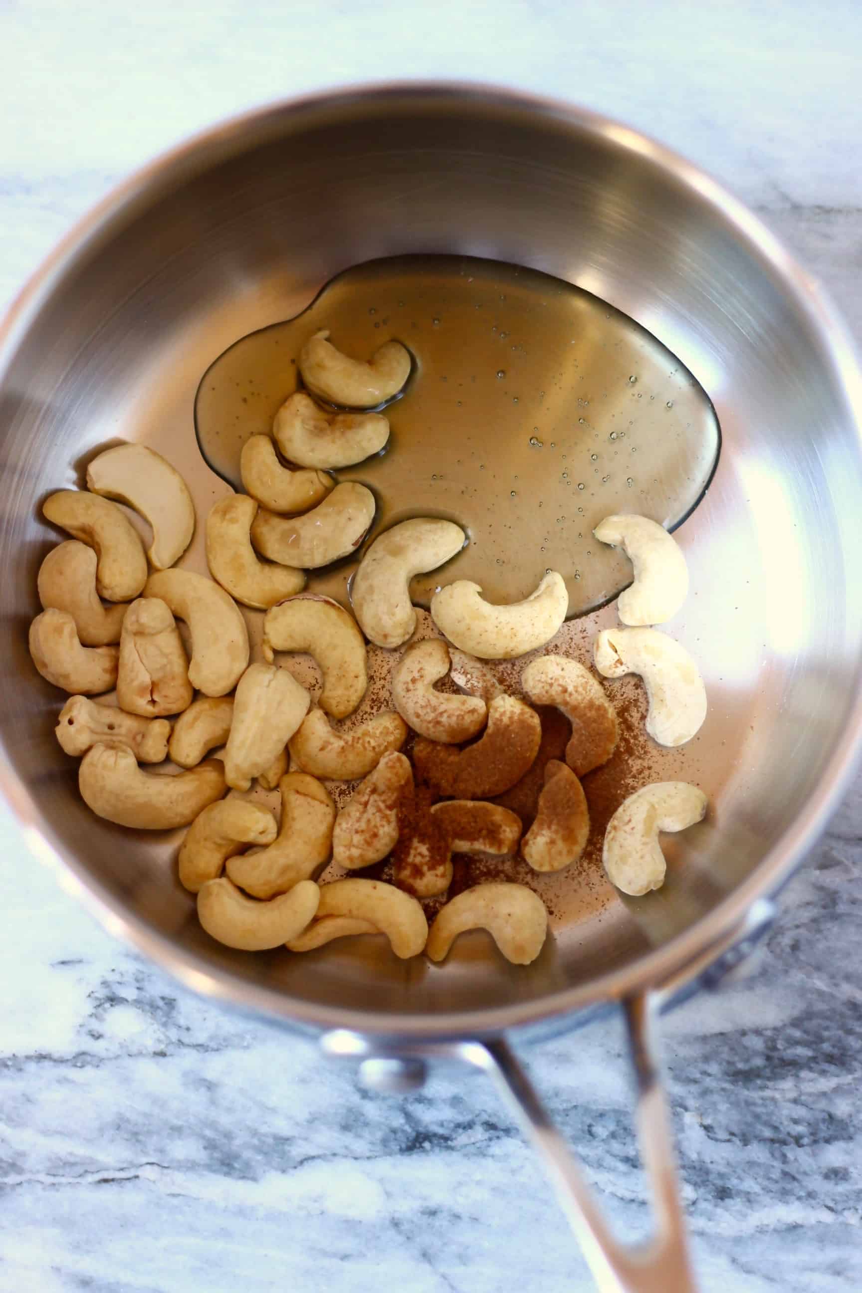Cashew nuts, maple syrup and ground spices in a pan against a marble background