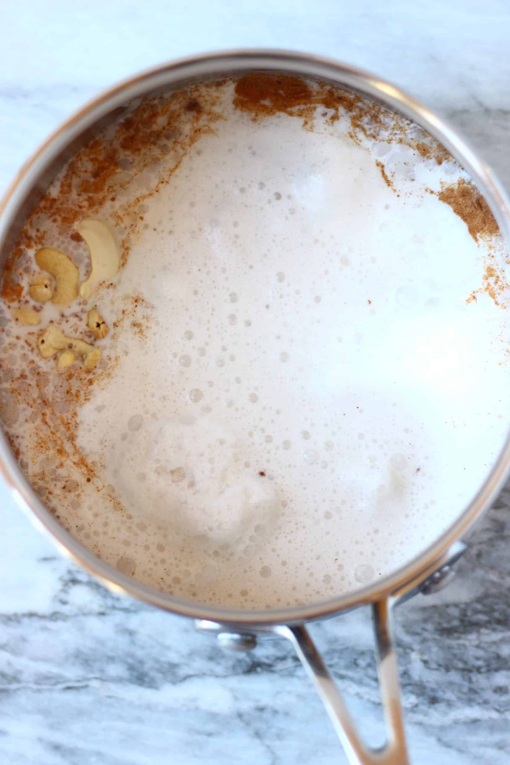 This Vegan Eggnog is super rich and creamy, so comforting and perfectly spiced. Dairy-free, gluten-free, egg-free, refined sugar free and healthier than the traditional version! The perfect festive drink for Christmas! #rhiansrecipes #dairyfree #glutenfree #vegan #christmas #eggnog #drink Plant-based milk and ground spices in a saucepan against a marble background