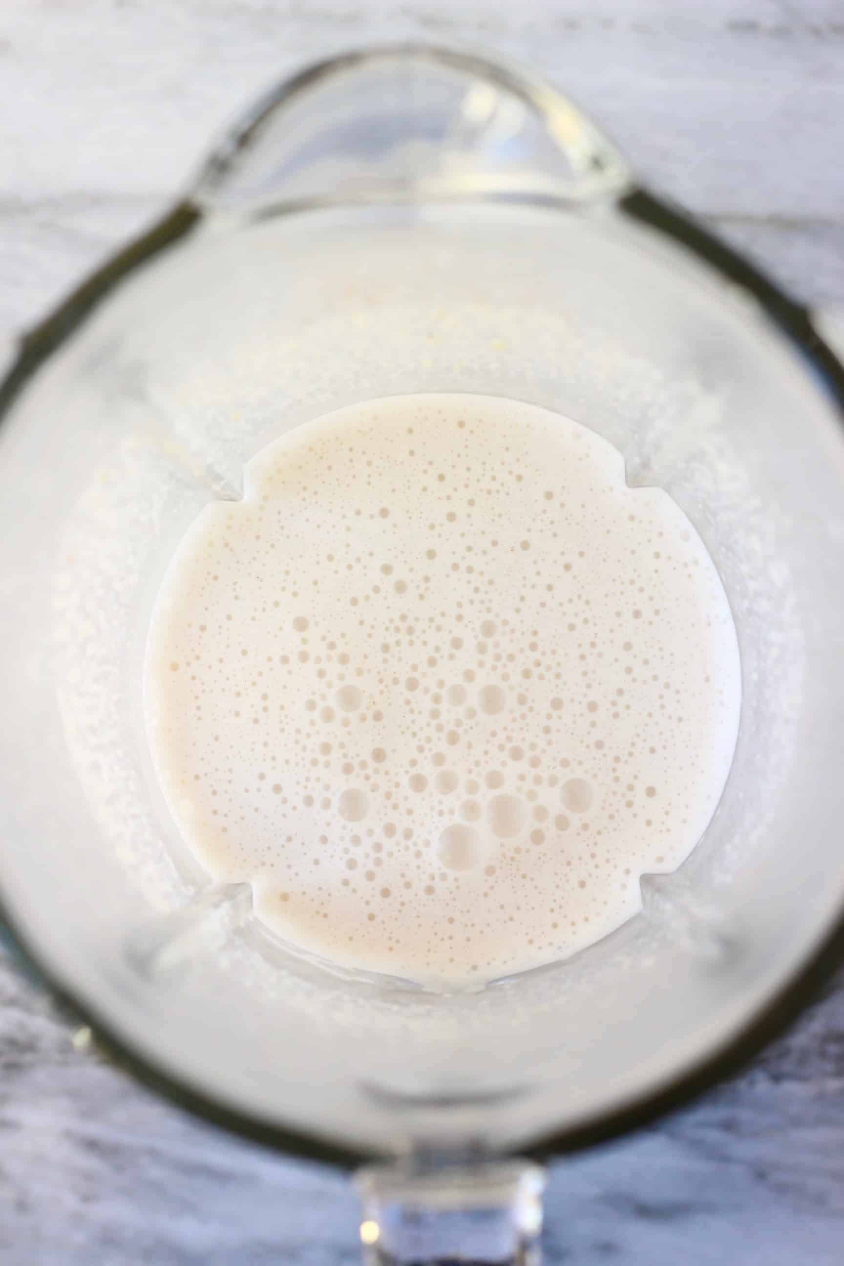 Plant-based milk, cashew nuts and ground spices in a blender against a marble background