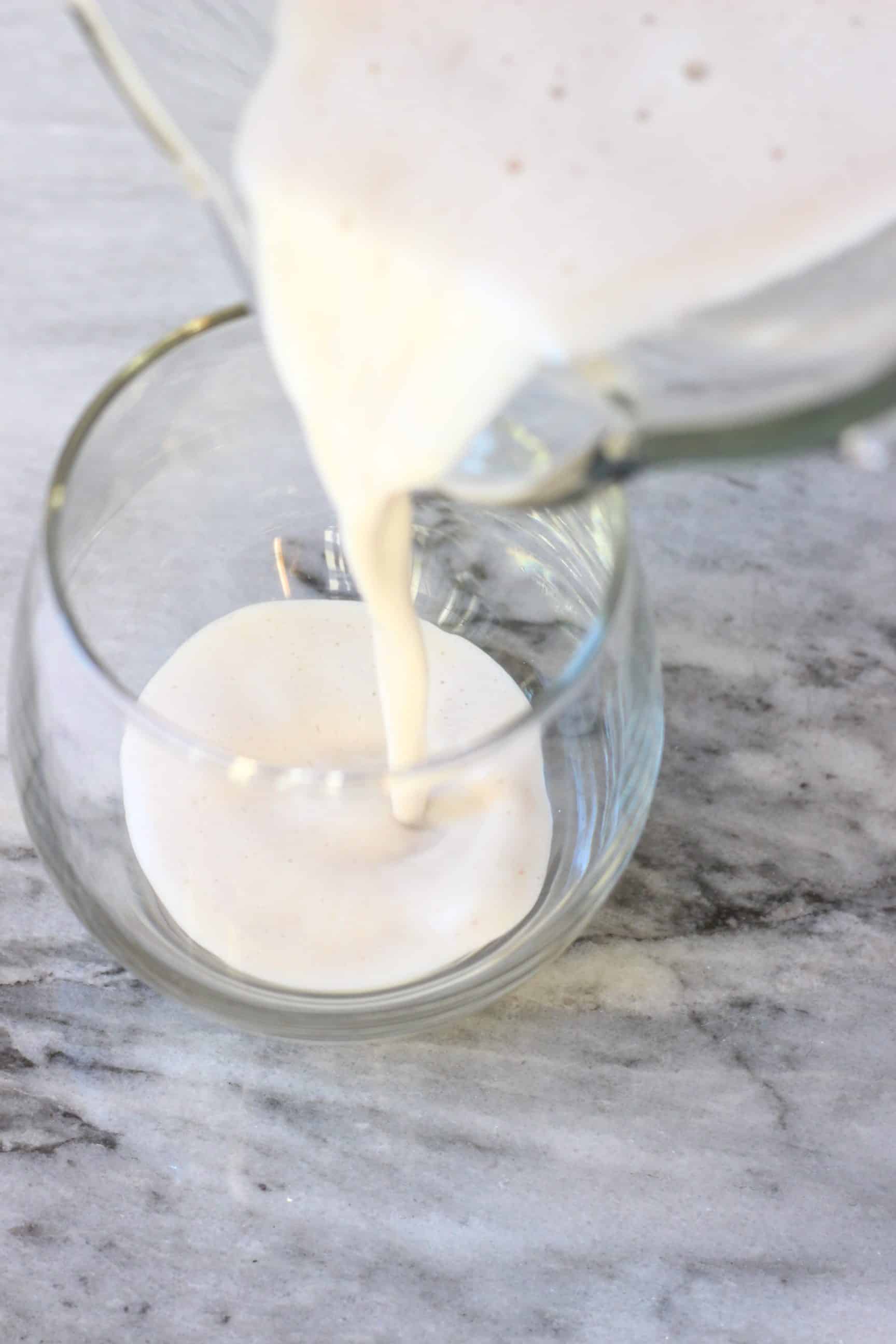 This Vegan Eggnog is super rich and creamy, so comforting and perfectly spiced. Dairy-free, gluten-free, egg-free, refined sugar free and healthier than the traditional version! The perfect festive drink for Christmas! #rhiansrecipes #dairyfree #glutenfree #vegan #christmas #eggnog #drink Vegan eggnog being poured into a glass from a blender