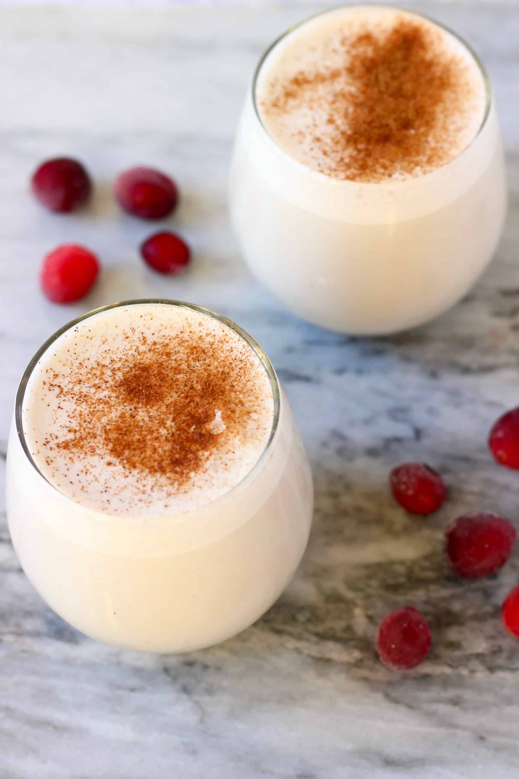 This Vegan Eggnog is super rich and creamy, so comforting and perfectly spiced. Dairy-free, gluten-free, egg-free, refined sugar free and healthier than the traditional version! The perfect festive drink for Christmas! #rhiansrecipes #dairyfree #glutenfree #vegan #christmas #eggnog #drink Two glasses of eggnog topped with cinnamon against a marble background