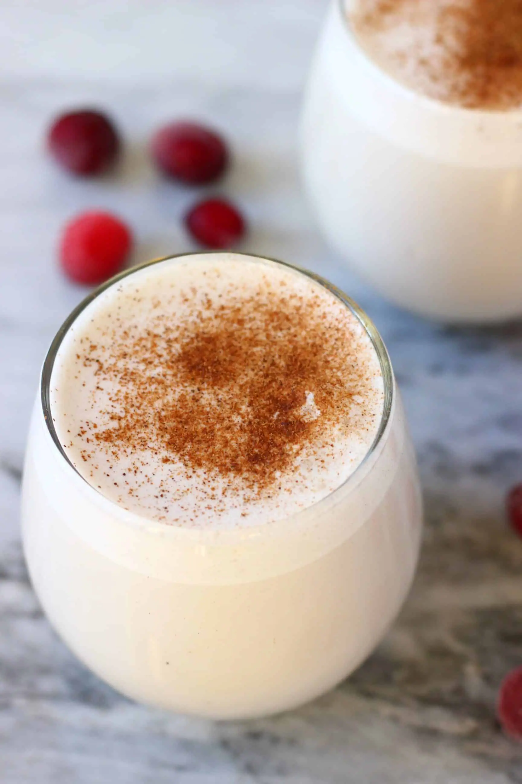 Two glasses of vegan eggnog topped with cinnamon against a marble background