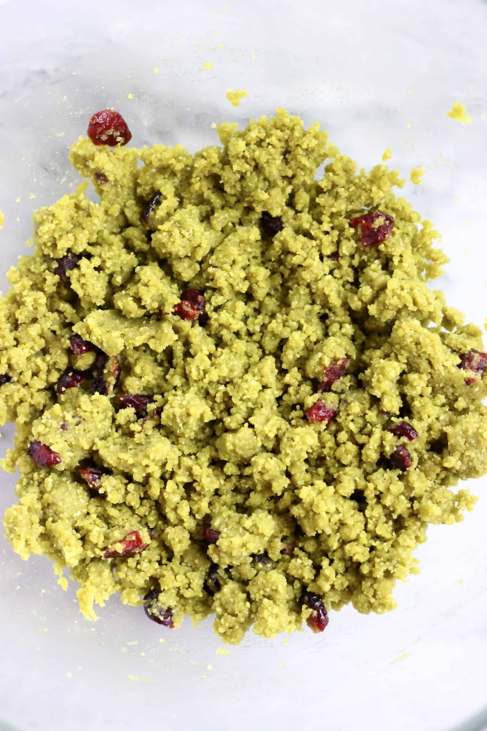 Raw vegan matcha shortbread cookie dough with dried cranberries in a mixing bowl