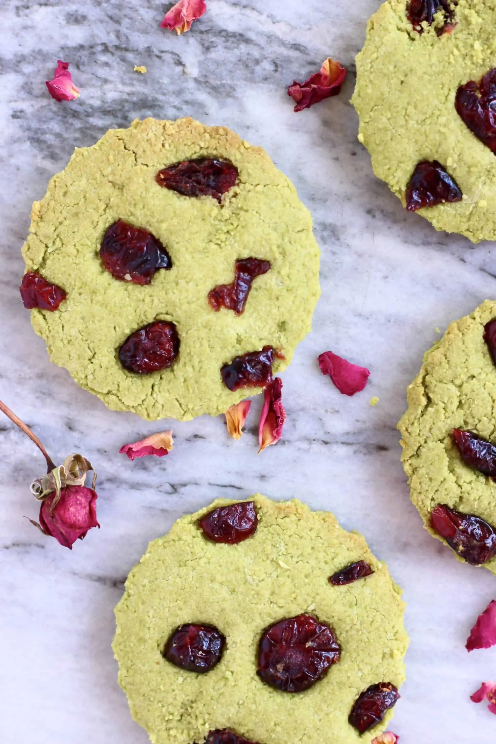 Four vegan matcha shortbread cookies with dried cranberries on a marble background