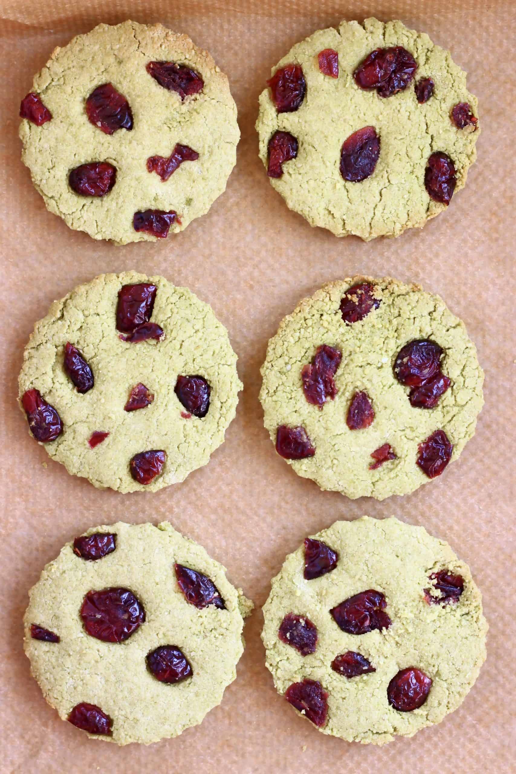 Six vegan matcha shortbread cookies with dried cranberries on a baking tray lined with baking paper