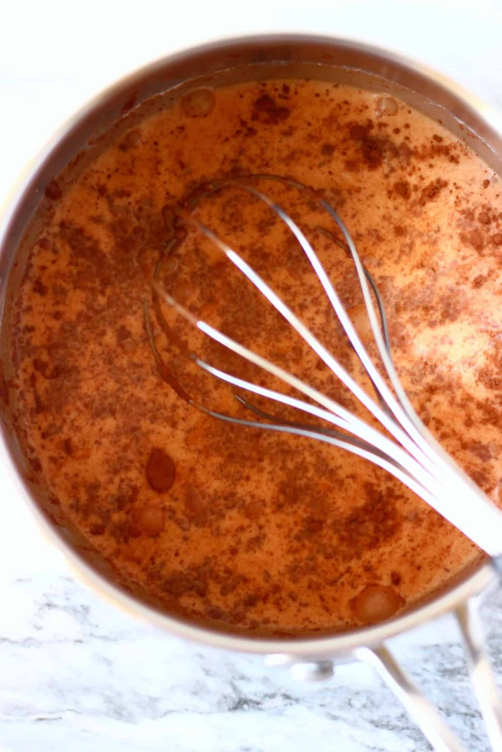Milk and cocoa powder in a pan being mixed with a balloon whisk 